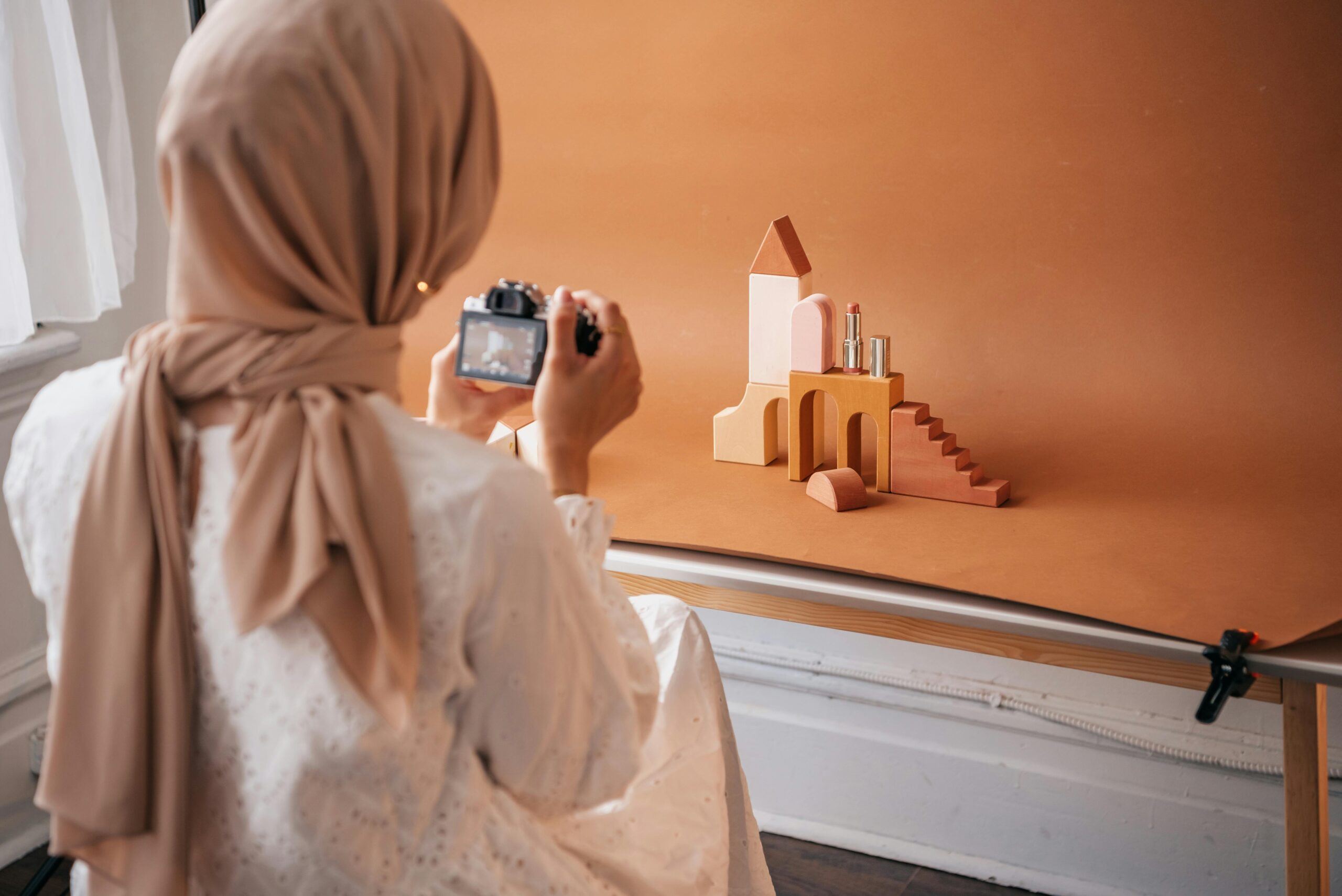 A woman takes a photo of beauty products with a camera in a studio setting. Neutral colors.